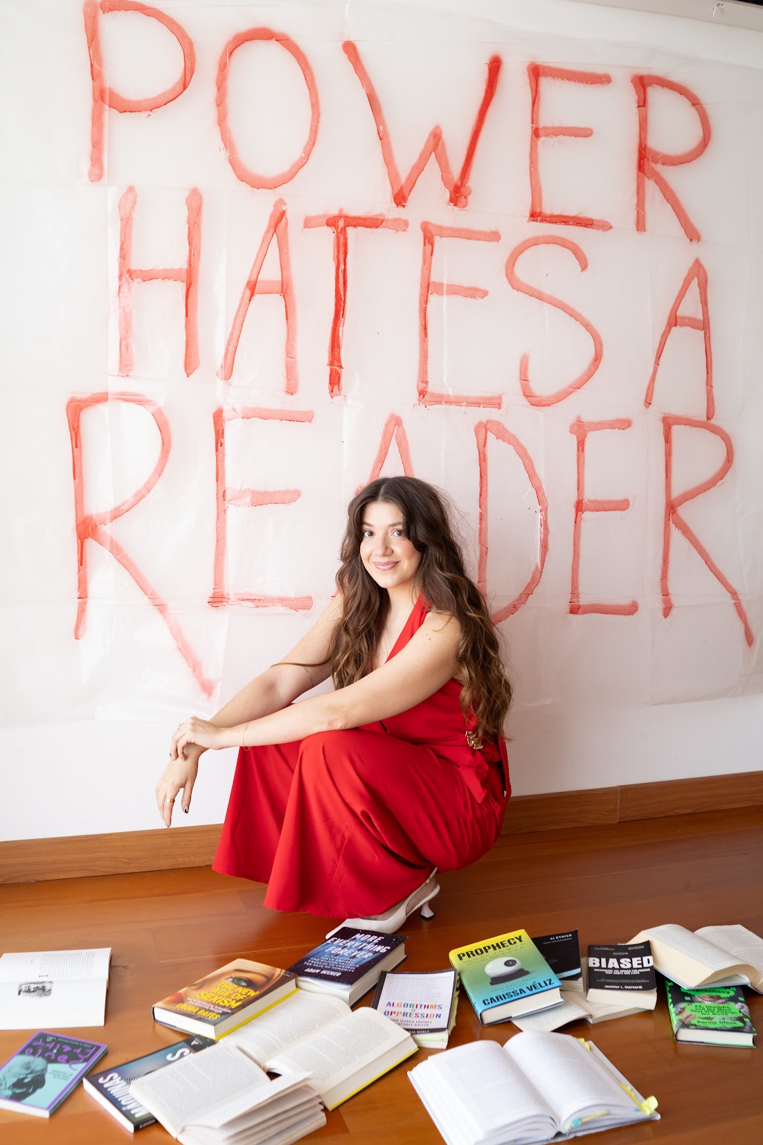 Catharina Doria, AI ethicist and founder of The AI Survival Club, in a red dress in front of a hand-painted Power Hates a Reader sign